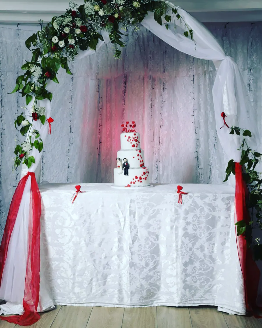 Pièce montée de mariage sous une arche de fleurs rouges